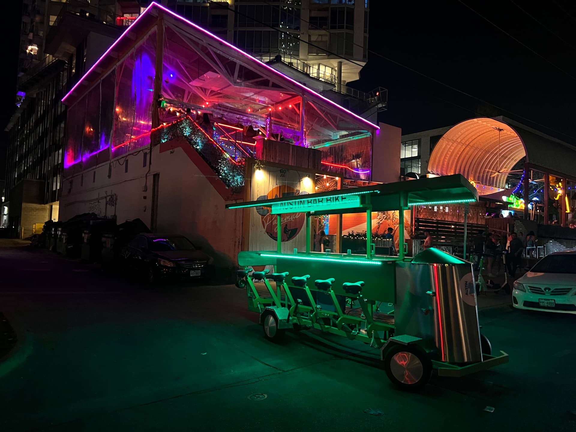 Green LED-lit BYOB party bike cruising 6th Street Austin at night